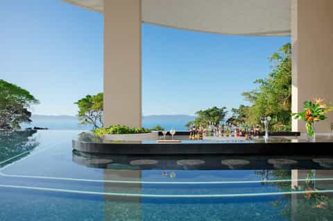 Elegant infinity bar overlooking an ocean view with lush greenery, the bar is seamlessly integrated into the landscape.