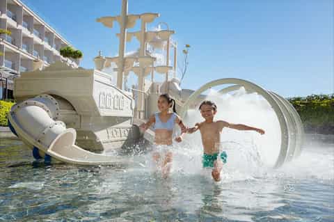 Children playing on elaborate ship-themed splash pad with water features and waterslides