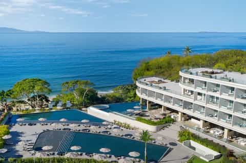 Multi-level resort with curved pools overlooking Mediterranean Sea and coastal landscape