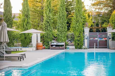 Modern lap pool surrounded by tall cypress trees, concrete deck, lounge chairs, and pool house structure