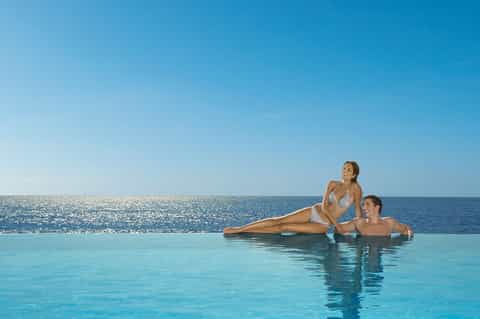 Couple relaxing in infinity pool with ocean horizon and clear blue sky blending seamlessly