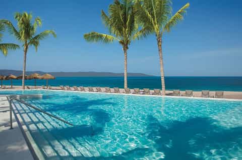 Turquoise pool with palm trees, beach umbrellas, ocean view, and lounge chairs