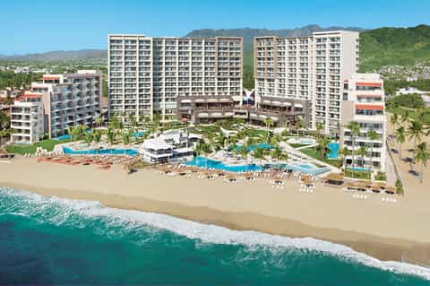 Beachfront all-inclusive resort with multiple towers, pools, and palm trees by shore
