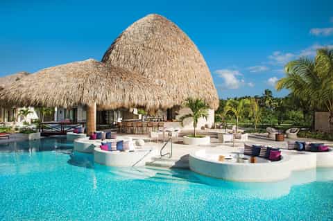 Luxury resort pool with thatched bungalows, in-pool lounging platforms, and palm trees