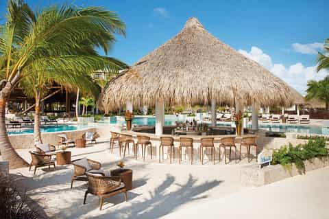 Beachside tiki bar with thatched roof, turquoise pool, and lounge seating
