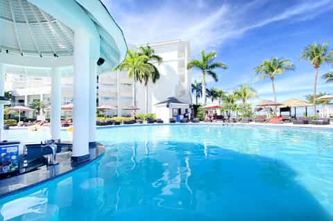 Indoor heated swimming pool with palm trees, white pergola, and multi-story hotel building