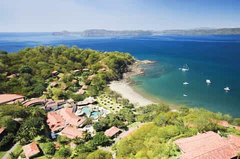 Aerial view of beachfront resort with pool overlooking tropical coastline