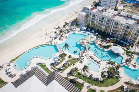 Aerial view of beachfront resort with multiple pools, sandy beach, and oceanfront buildings