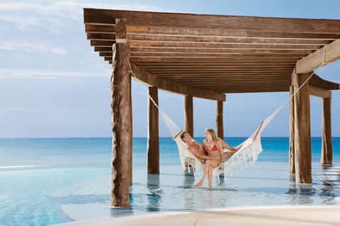 Couple relaxing in white hammock under wooden pergola overlooking turquoise ocean