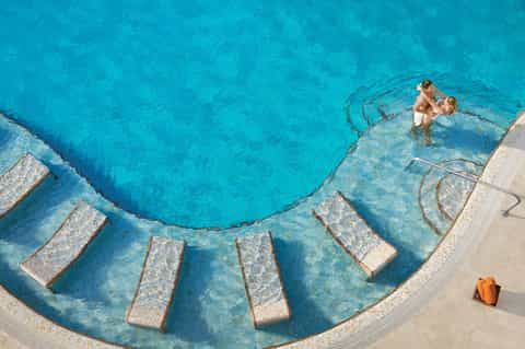 Aerial view of curved luxury swimming pool with submerged loungers and turquoise water