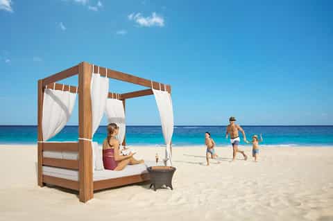 Woman relaxing in beachfront cabana with family swimming in turquoise ocean