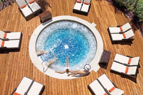 Overhead view of circular hot tub surrounded by lounge chairs on wooden deck with landscaping