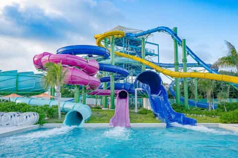 Colorful water park with multiple slides in pink, blue, and yellow entering bright blue pool