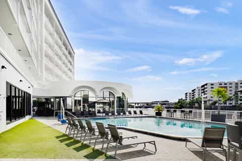 Modern resort pool area with lounge chairs, white building, and waterfront views