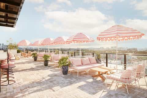Rooftop lounge with pink striped umbrellas, white furniture, and city skyline views