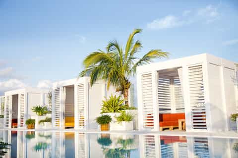 Modern resort cabanas with white louvered walls, orange cushions, and reflection pool