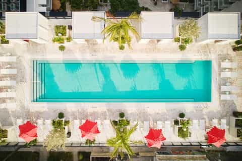 Aerial view of resort pool with turquoise water, red lounge chairs, and white cabanas