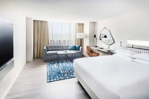 Modern hotel suite with bed, sofa, desk, floor-to-ceiling windows with neutral décor