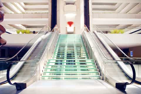 Modern mall staircase with glass steps, escalators, and red hanging art installation