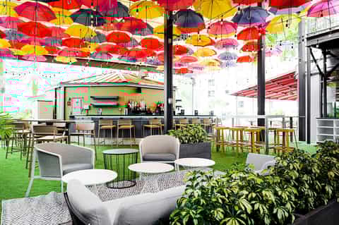 Rooftop dining venue with colorful umbrellas overhead, green turf, comfortable seating, and bar area