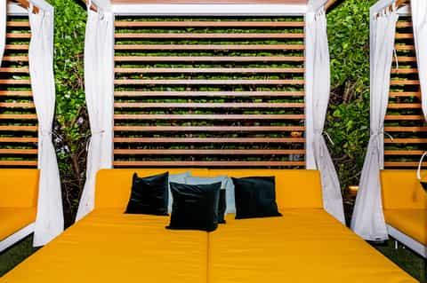 Luxury cabana bed with golden frame, white drapes, and black pillows outdoors