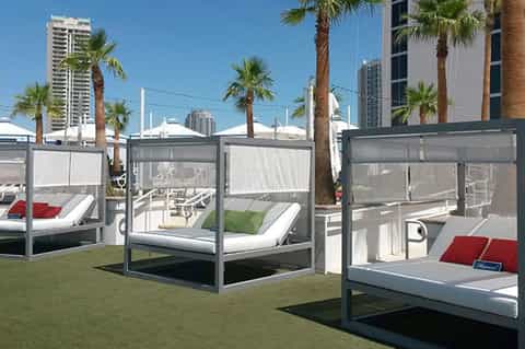 Modern resort cabana beds with privacy curtains on grass with palm trees and cityscape