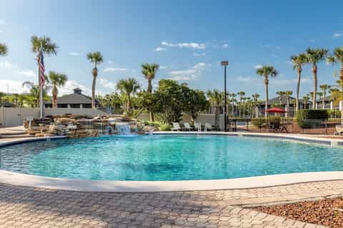 Lagoon-style pool with rock waterfall feature, surrounded by palm trees and manicured grounds