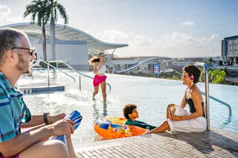Family enjoying rooftop infinity pool with city skyline and palm trees in background