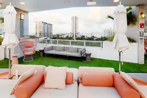Modern rooftop lounge with city views, orange seating, white umbrellas, and artificial grass