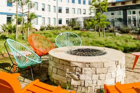 Modern courtyard with fire pit, colorful wire chairs, and contemporary residential buildings