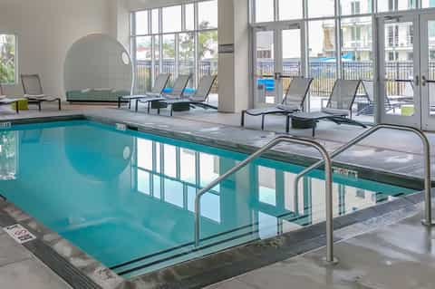 Indoor heated pool with loungers, glass doors leading to outdoor deck, and ocean view windows