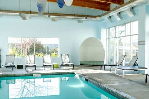 Indoor pool area with light blue walls, wooden beams, lounge chairs, and large egg-shaped seating pod