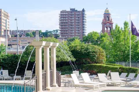 Elegant poolside area with classical columns, white lounge chairs, and urban skyline with church tower