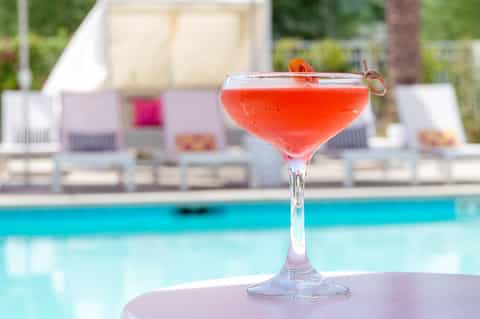 Coral-colored cocktail with fruit garnish on table by resort pool deck
