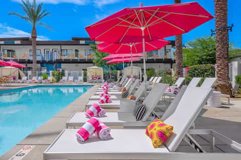 Resort pool with bright pink umbrellas, white lounge chairs, and palm trees lining deck