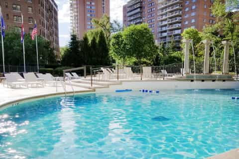 Urban rooftop pool with clear water, lounge chairs, and city apartment buildings in background