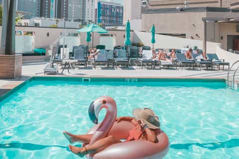 Urban rooftop pool with flamingo float, turquoise water, and downtown city skyline at daytime