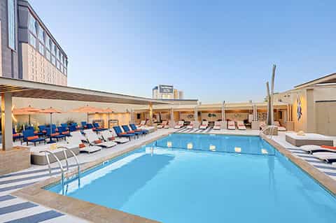 Rooftop pool deck with colorful lounge chairs, umbrellas, surrounding high-rise hotel building under clear blue sky