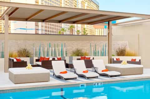 Modern poolside lounge with chaise lounges, pergola shade, and high-rise hotel backdrop