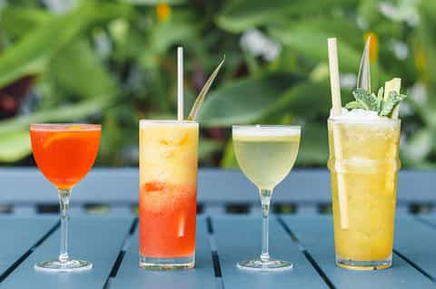 Four colorful cocktails on dark deck with green garden background
