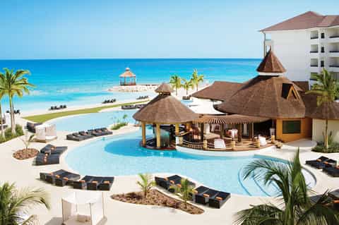 Beachfront resort pool complex with tiki bar, loungers, and ocean view with white sand beach