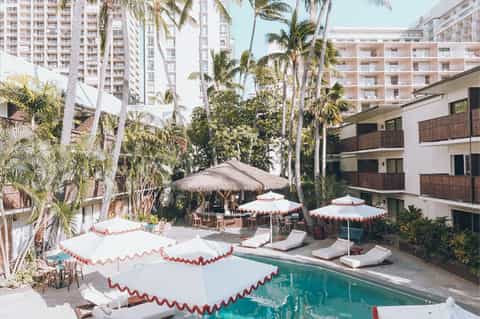 Resort pool courtyard with red and white umbrellas, palm trees, and high-rise buildings