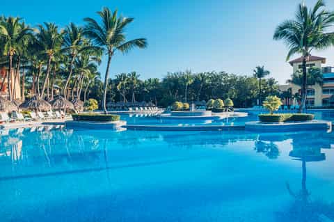 Resort infinity pool with bright blue water, palm trees, and white lounge chairs at sunset