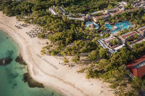 Aerial beachfront resort view with pool area, lounge chairs, palm trees, and white sand beach