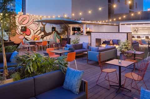 Upscale rooftop lounge at dusk with colorful art, modern seating, ambient lighting, and decorative pillows