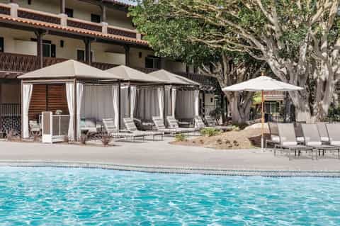 Resort pool area with cabanas, lounge chairs, and large shade umbrellas near Spanish colonial architecture