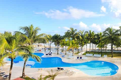 Aerial view of large curved resort pool surrounded by palm trees and sandy beach