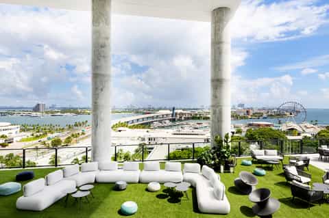 Modern lounge with curved white seating, colorful cushions, concrete pillars, and expansive water view
