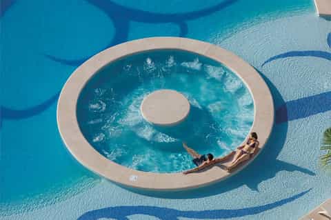 Aerial view of circular resort pool with two guests relaxing on deck