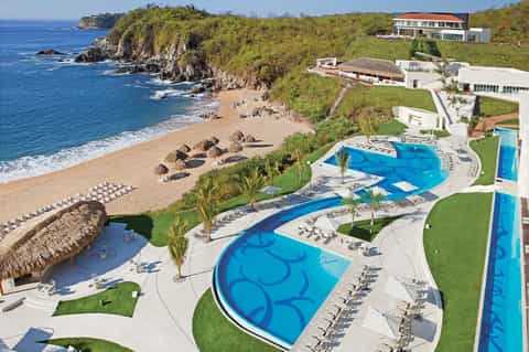 Luxury cliff-top resort with multiple pools overlooking ocean beach and tropical landscape